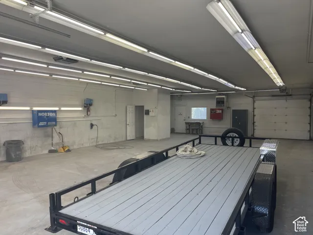 Spacious multi-car garage featuring overhead linear lighting, concrete flooring, painted masonry walls, and a dedicated wall-mounted climate control unit