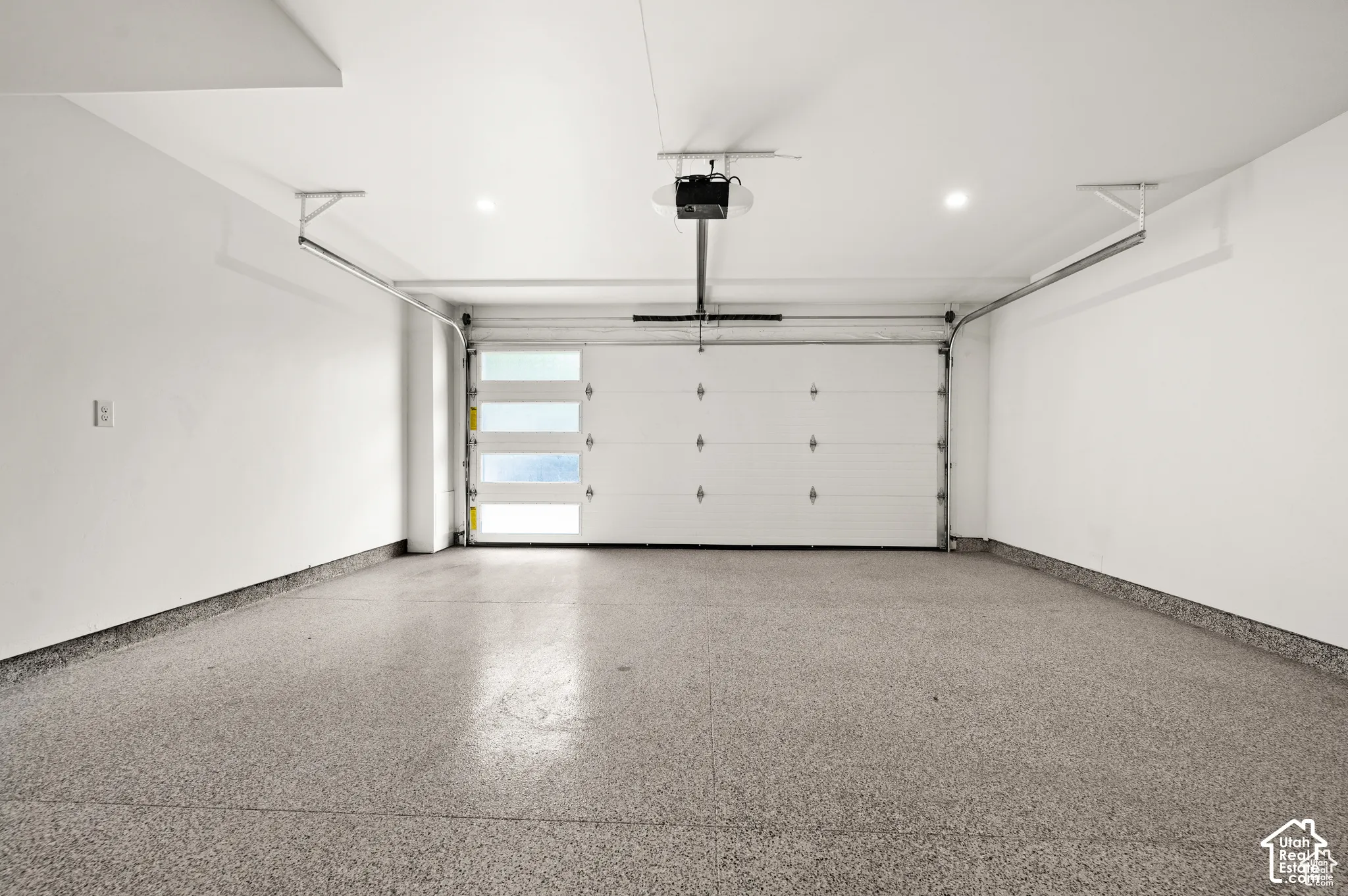 Attached garage featuring finished epoxy flooring, white paneled walls, ceiling-mounted recessed lighting, and a sectional door with frosted glass windows