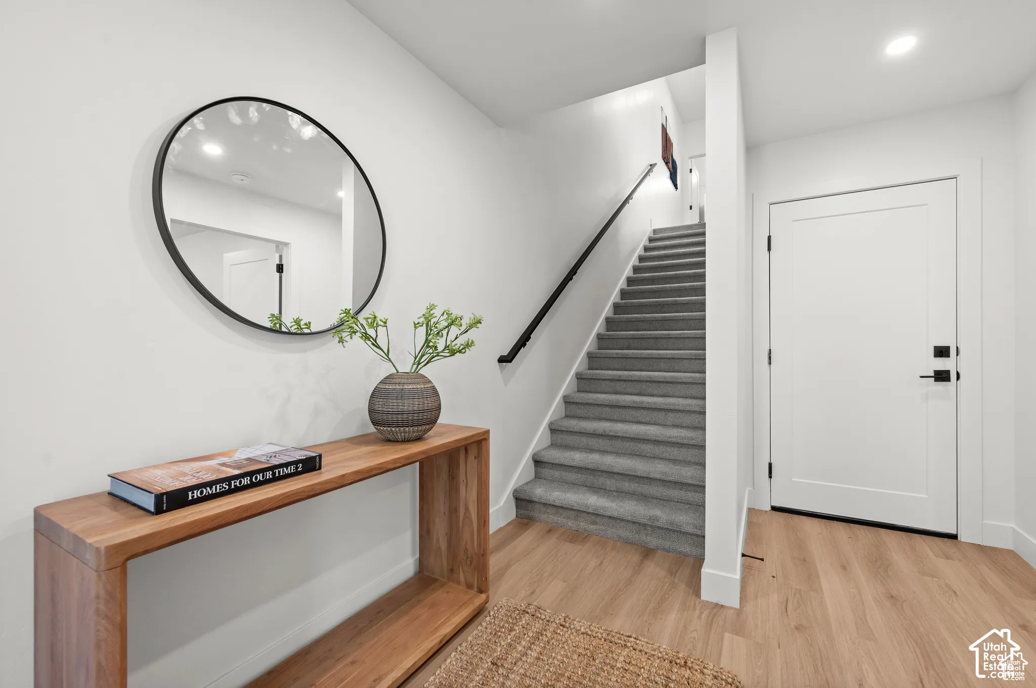 Entryway featuring wood-finish flooring, a staircase with carpeted treads, a wall-mounted matte black handrail, and a recessed ceiling light