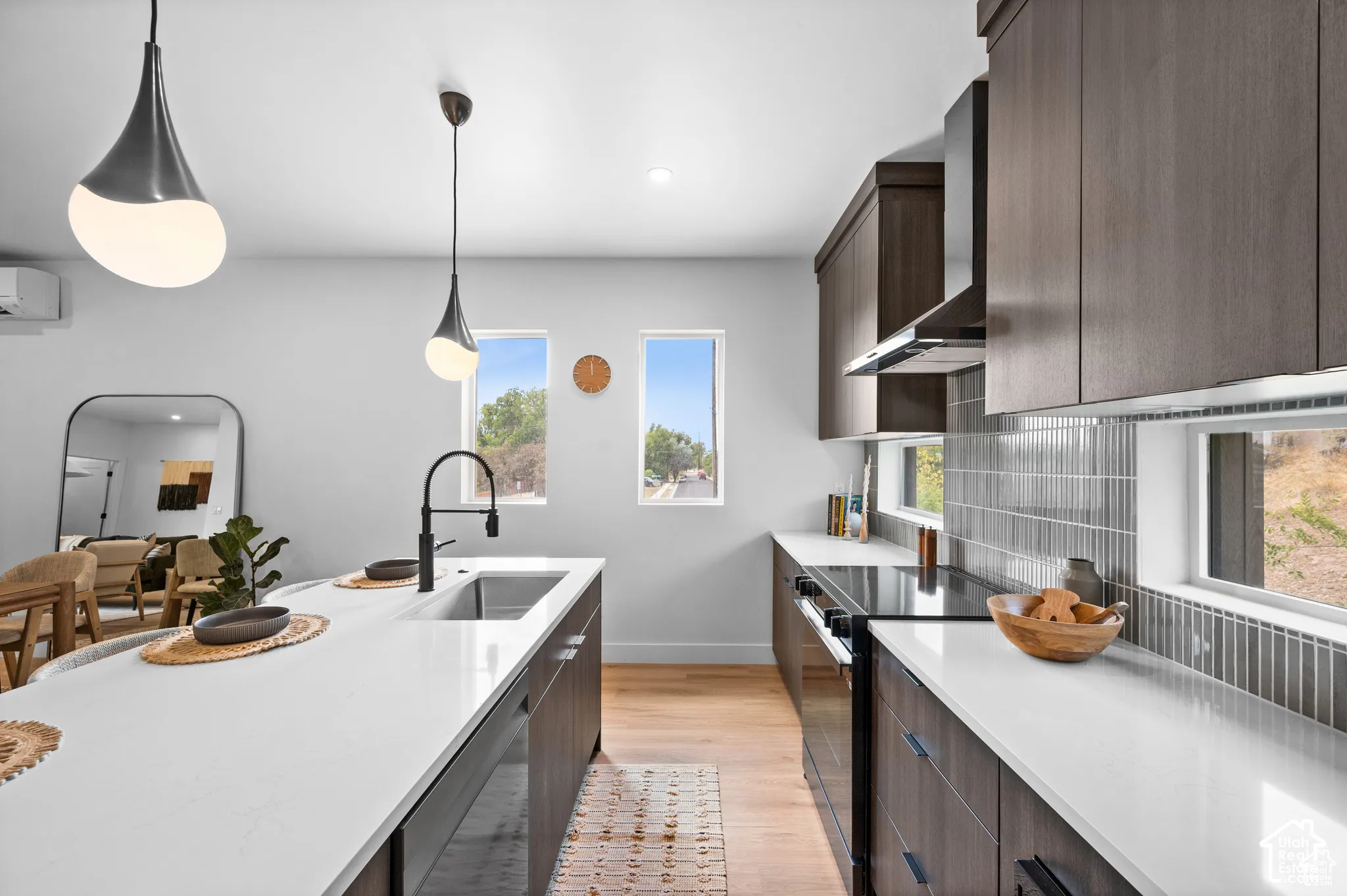 Kitchen featuring dark wood cabinetry, white countertops, vertical tile backsplash, wood-finish flooring, and pendant lighting