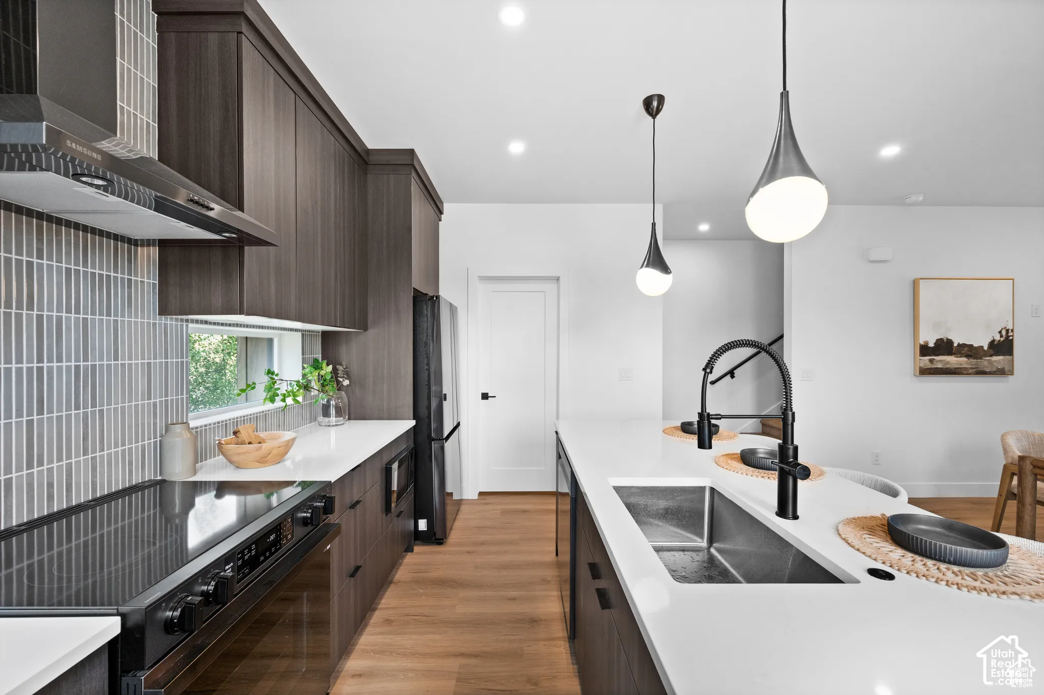 Kitchen featuring dark wood-finish cabinetry, quartz countertops, vertical tile backsplash, stainless steel undermount sink with matte black faucet, and modern pendant lighting
