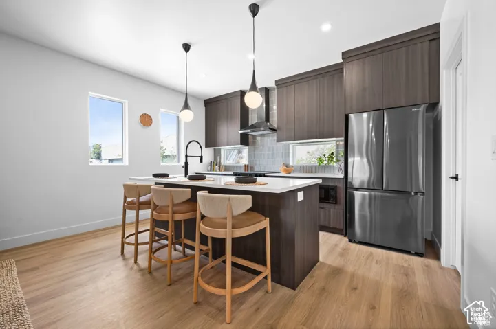 Kitchen featuring dark wood-finish cabinetry, white countertops, stainless steel appliances, a tile backsplash, and two pendant lights above the central island