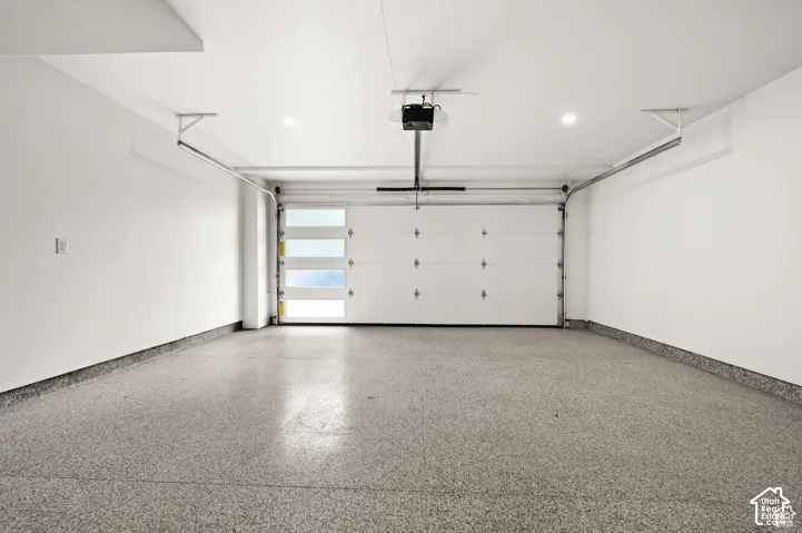Attached garage featuring finished epoxy flooring, white paneled walls, ceiling-mounted recessed lighting, and a sectional door with frosted glass windows