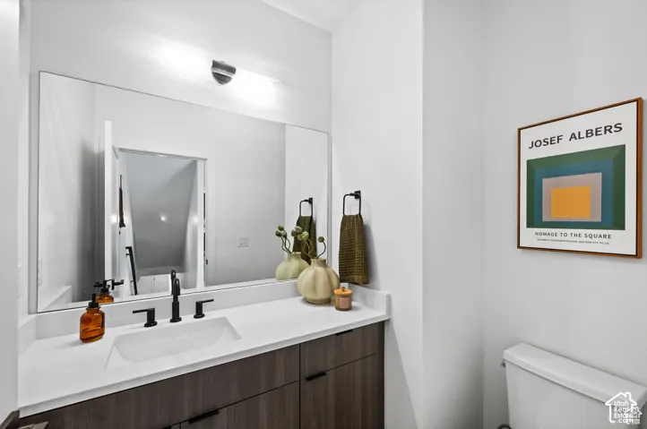 Wall-mounted lighting fixture above a large vanity mirror, dark wood-finish cabinetry, white countertop with an integrated rectangular sink, and matte black plumbing fixtures