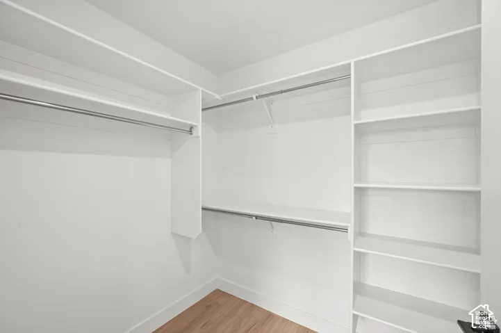 Walk-in closet featuring white built-in shelving, integrated hanging rods, and wood-finish flooring