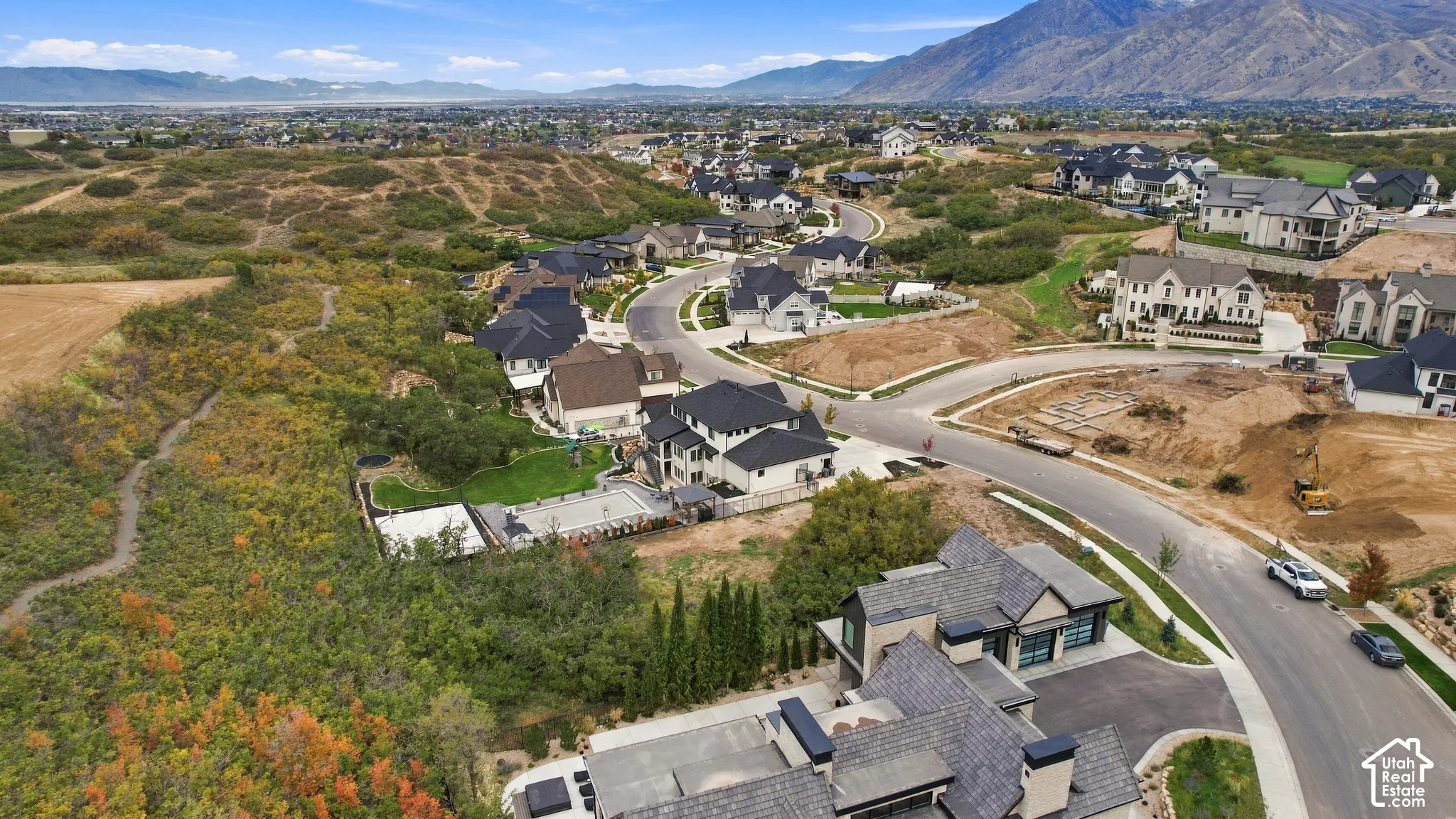 Aerial perspective of a multi-level residence featuring a multi-car garage, asphalt driveway, complex multi-pitch roofline, and mountain backdrop