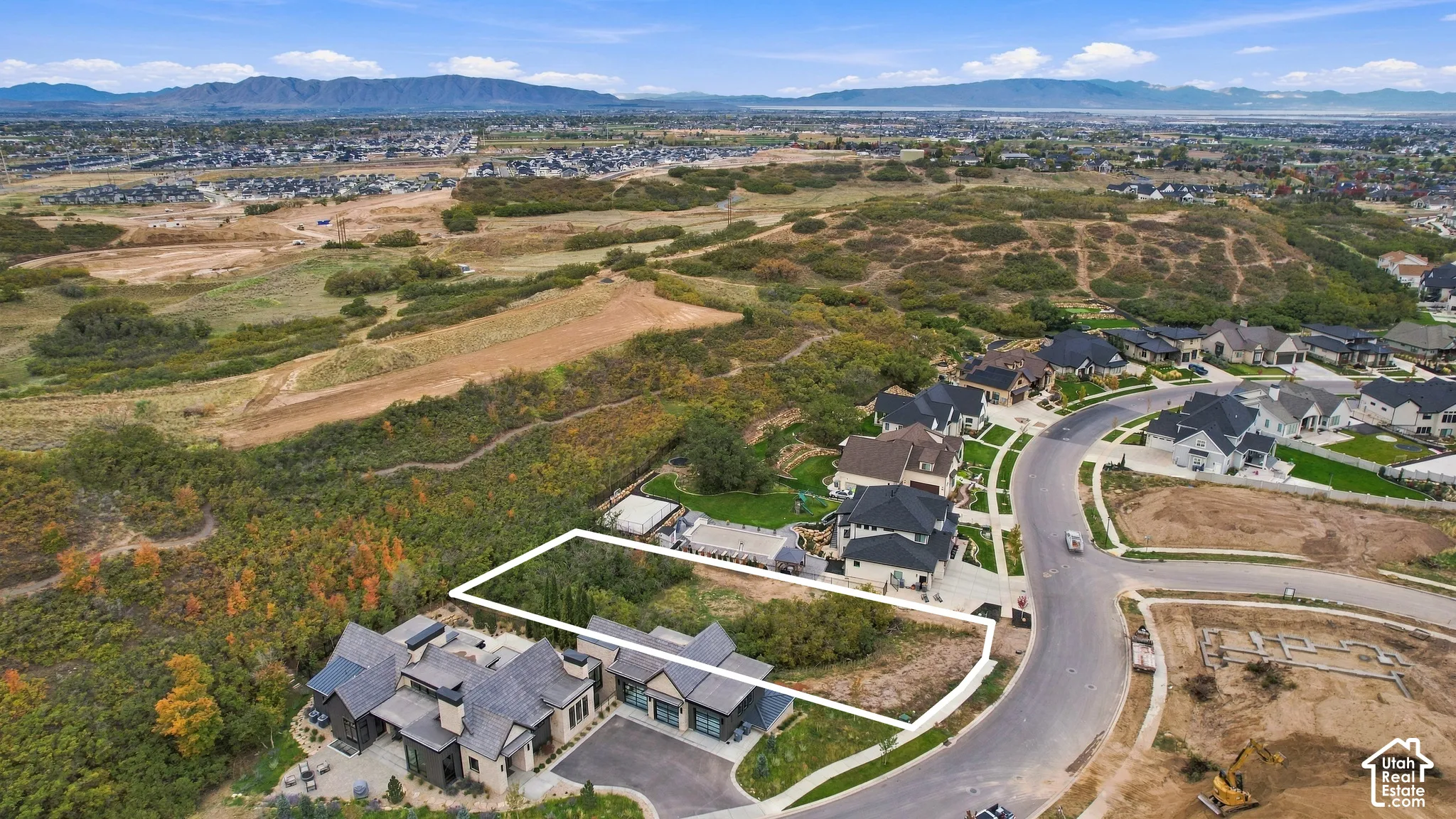 Aerial perspective of a multi-structure property featuring dark gabled roofing, stone and stucco exterior cladding, a paved driveway, and expansive hillside terrain with mountain backdrops
