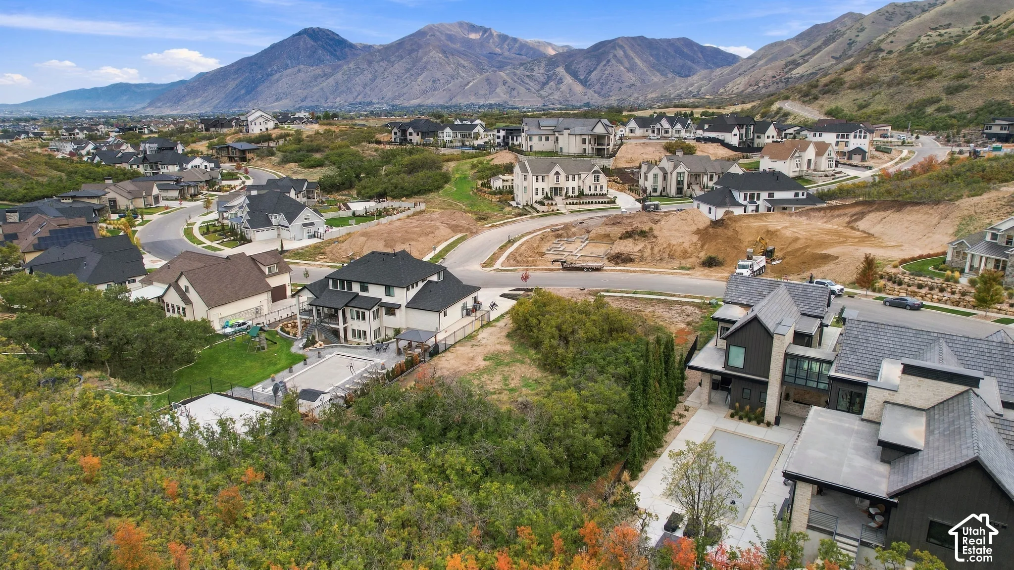 Aerial perspective of a hillside residential community featuring multi-story dwellings, paved roadways, residential swimming pools, and prominent mountain backdrops