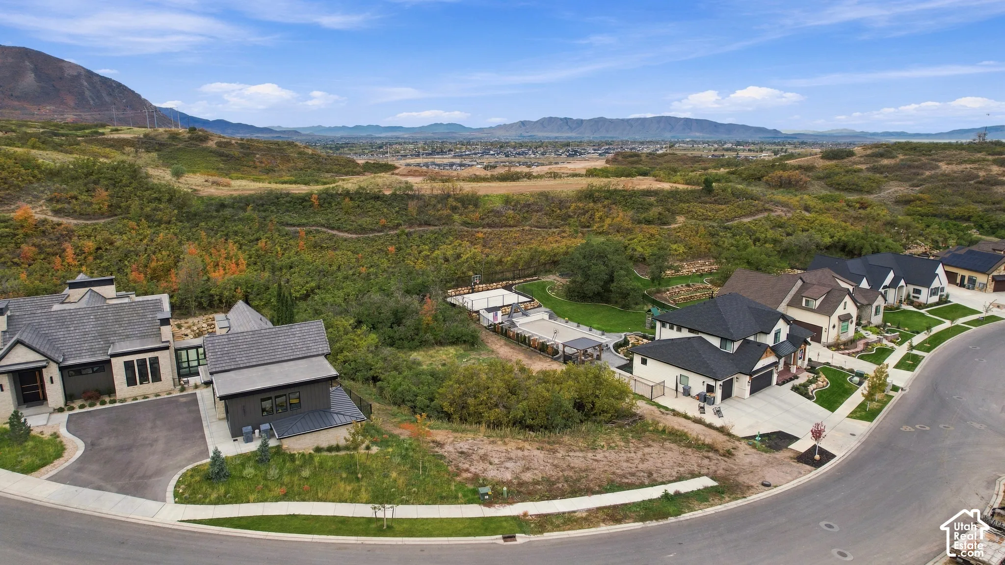Aerial perspective of hillside properties featuring expansive mountain scenery, paved driveways, multi-pitched rooflines, and manicured landscaping