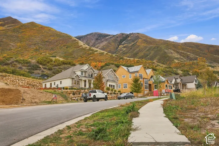 Streetscape featuring multi-story residential architecture with stone and wood-finish siding, concrete sidewalk, and a prominent mountain backdrop