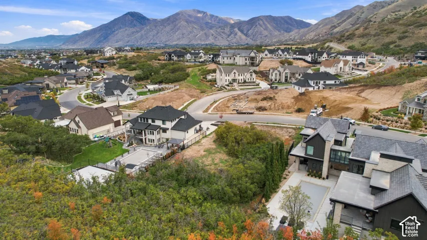 Aerial perspective of a hillside residential community featuring multi-story dwellings, paved roadways, residential swimming pools, and prominent mountain backdrops