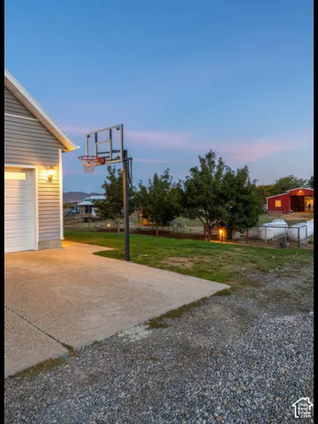Concrete driveway leading into the 3-car garage with integrated basketball hoop and exterior garage lighting.