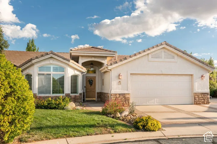 Single-story residence featuring a stucco and stone exterior, tile roofing, arched entryway, and an attached two-car garage