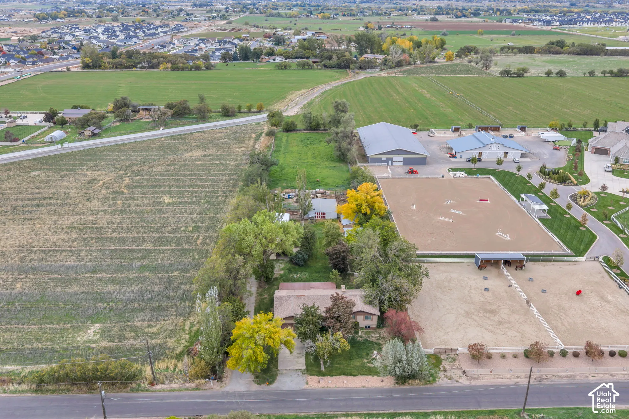Aerial perspective of expansive acreage featuring multiple equestrian riding arenas, a detached multi-bay shop, mature trees, and open pastureland