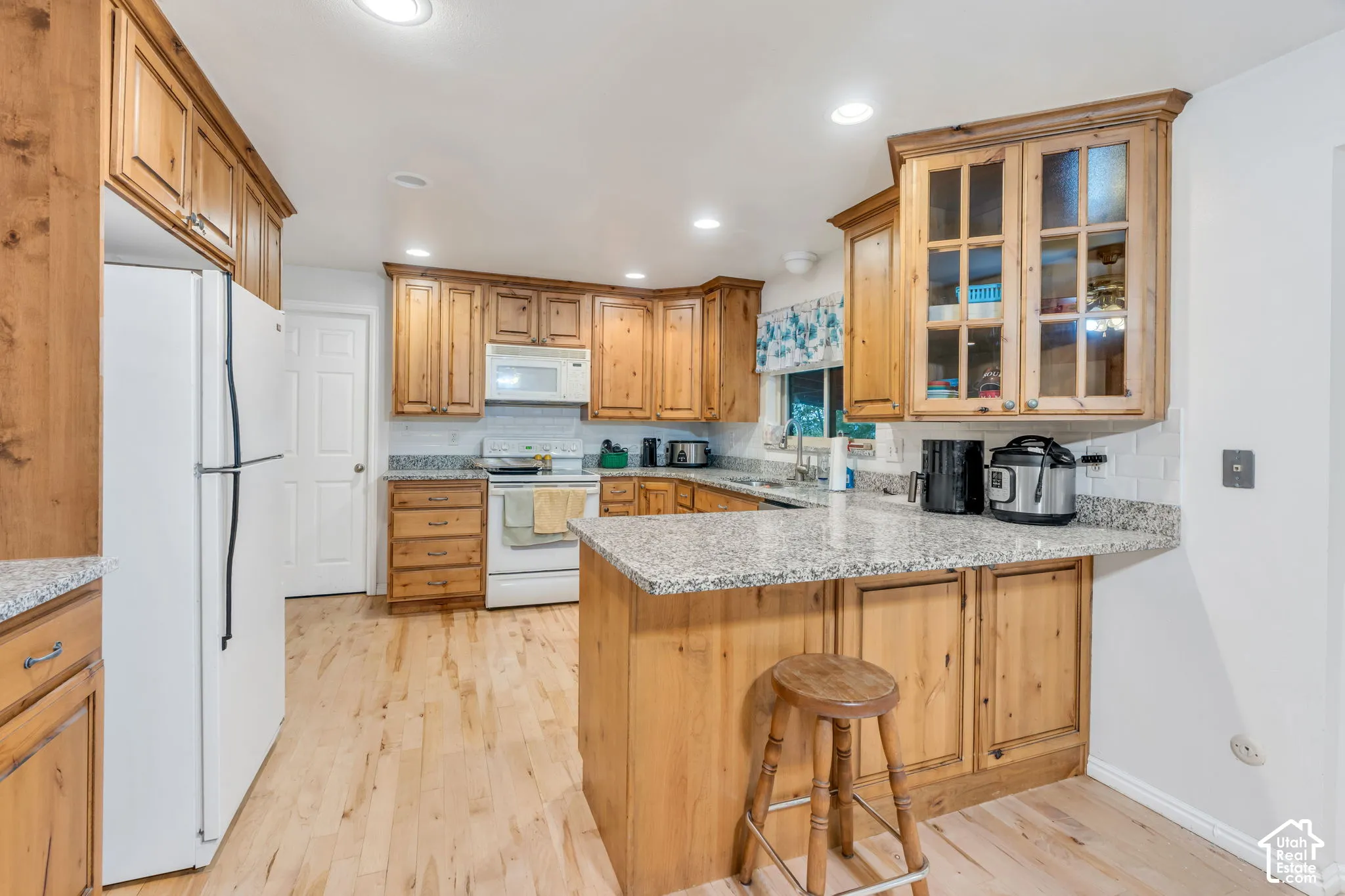 Kitchen featuring knotty wood cabinetry, stone countertops, wood-finish flooring, recessed lighting, and upper cabinets with glass-paneled doors