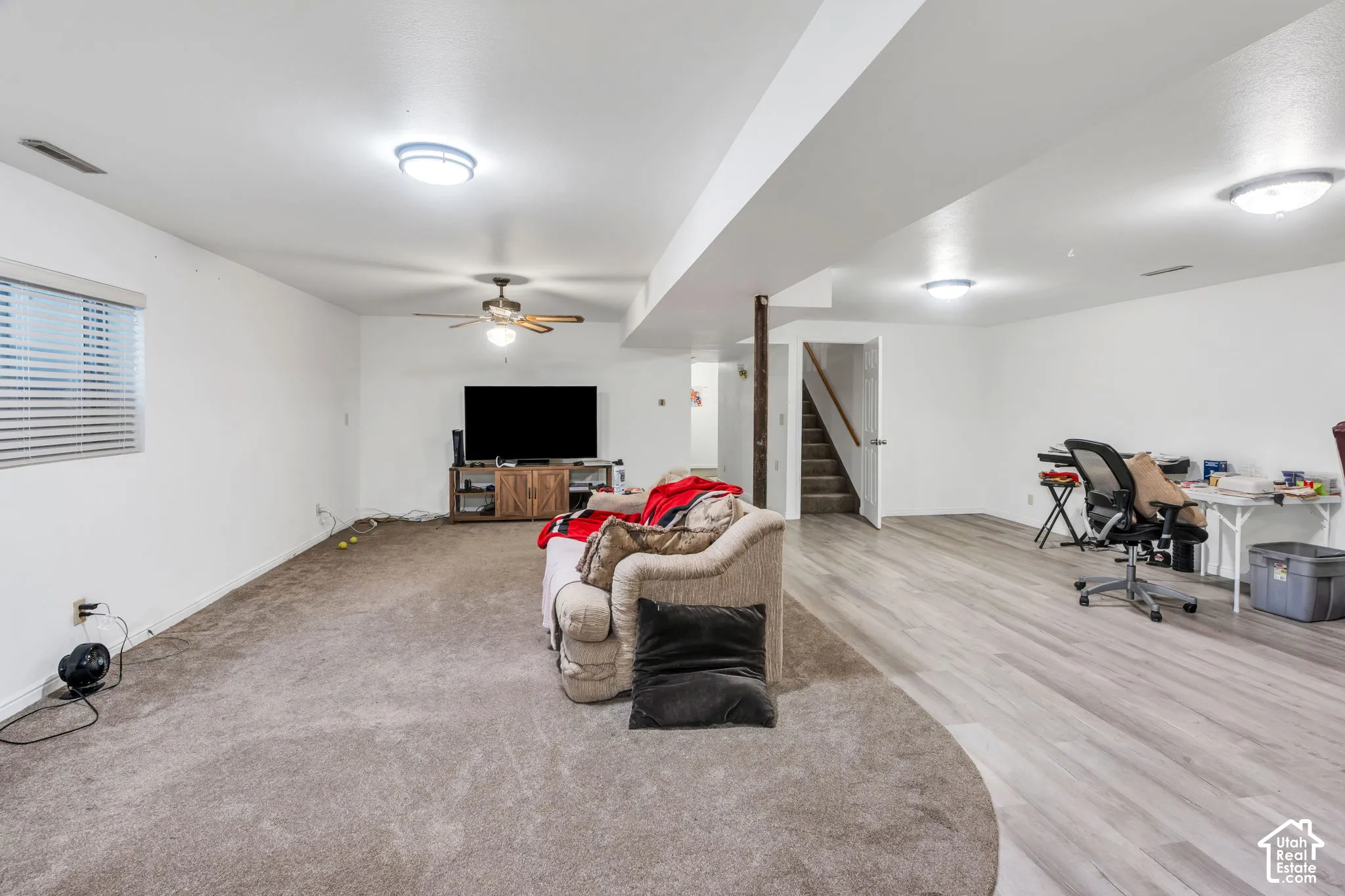 Expansive lower-level space featuring wood-finish flooring, wall-to-wall carpeting, a central ceiling fan with integrated lighting, and flush-mount ceiling fixtures