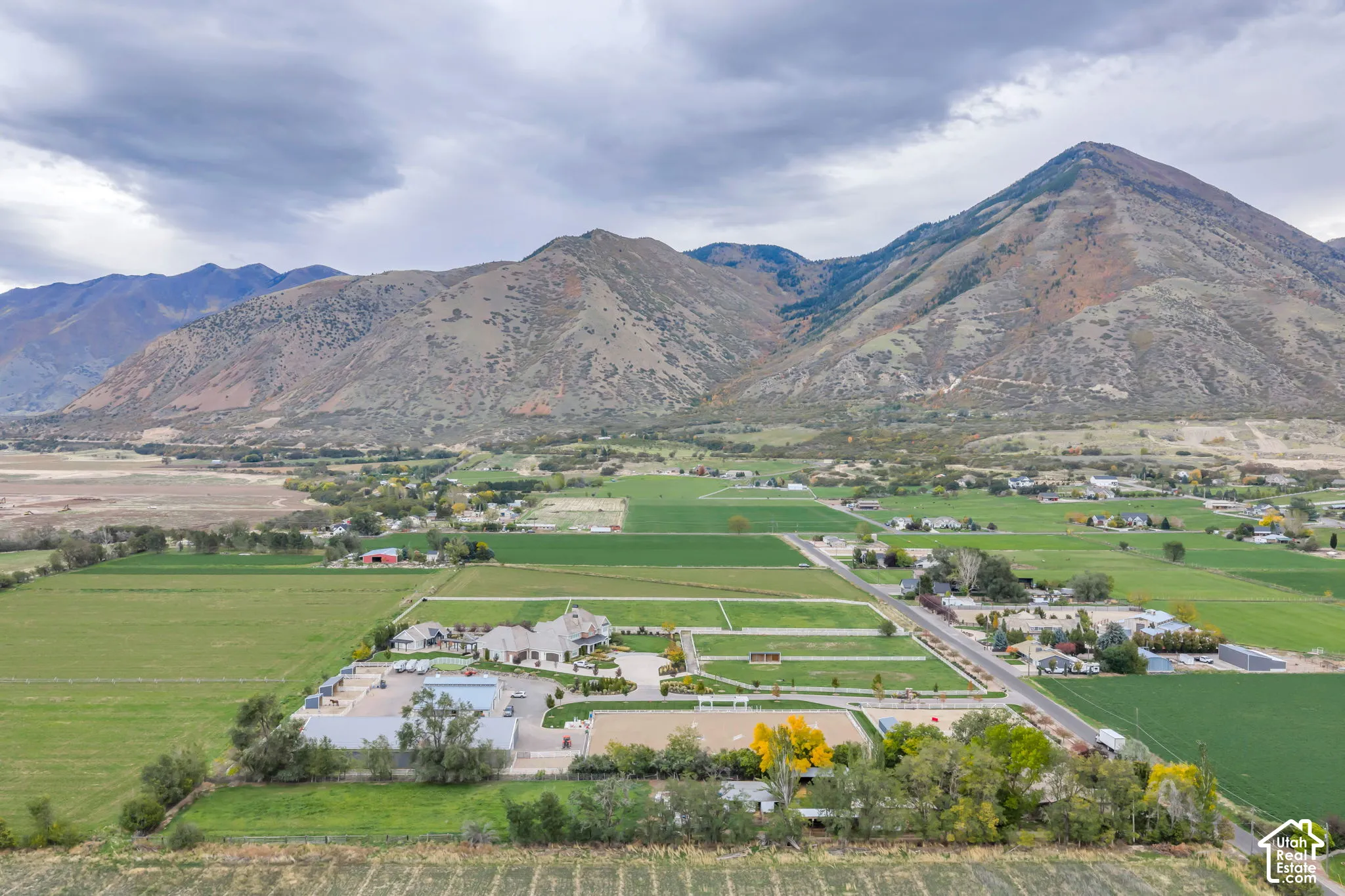 Aerial perspective of a sprawling property featuring mountain scenery, large-scale pasture land, a multi-structure building configuration, and outdoor riding arenas