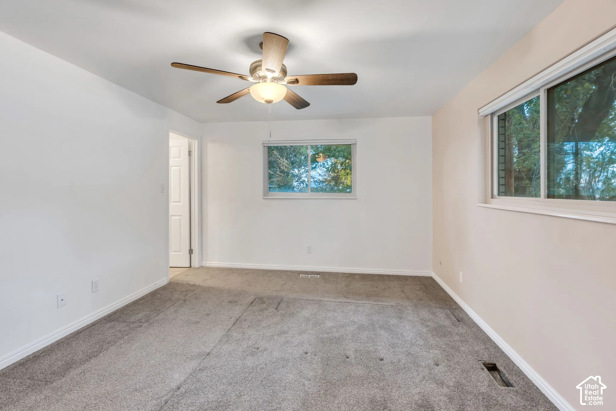 Neutral-toned carpeted flooring, dual windows with blinds, and a central ceiling fan with integrated lighting