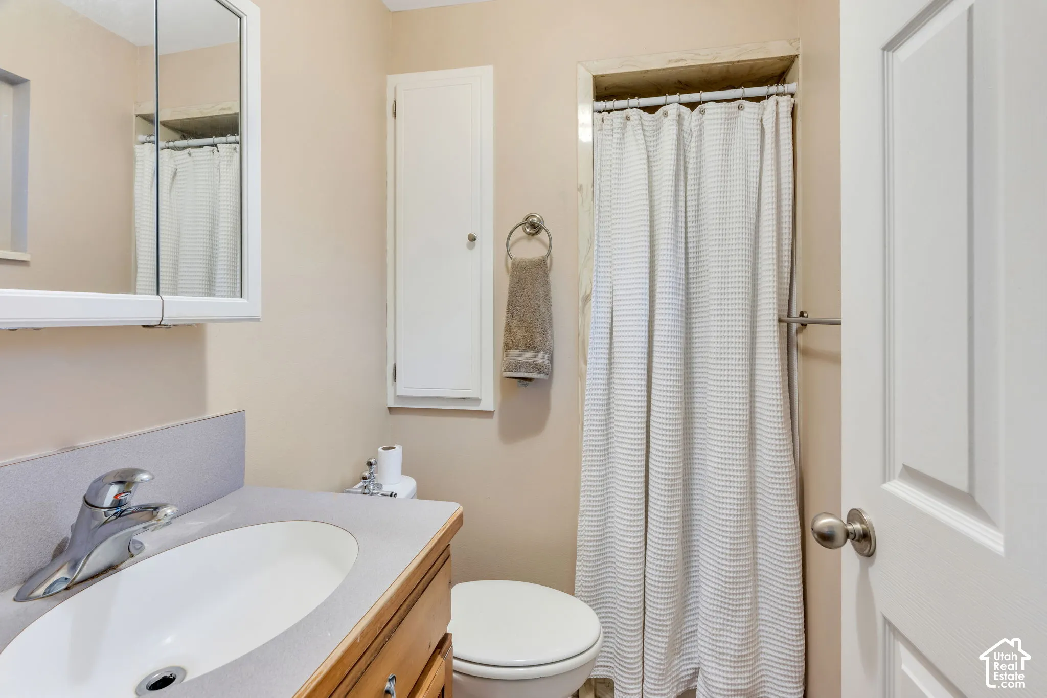 Bathroom featuring a wood-finish vanity with a solid-surface countertop and integrated sink, mirrored medicine cabinet, built-in wall cabinetry, and a shower with a curtain rod
