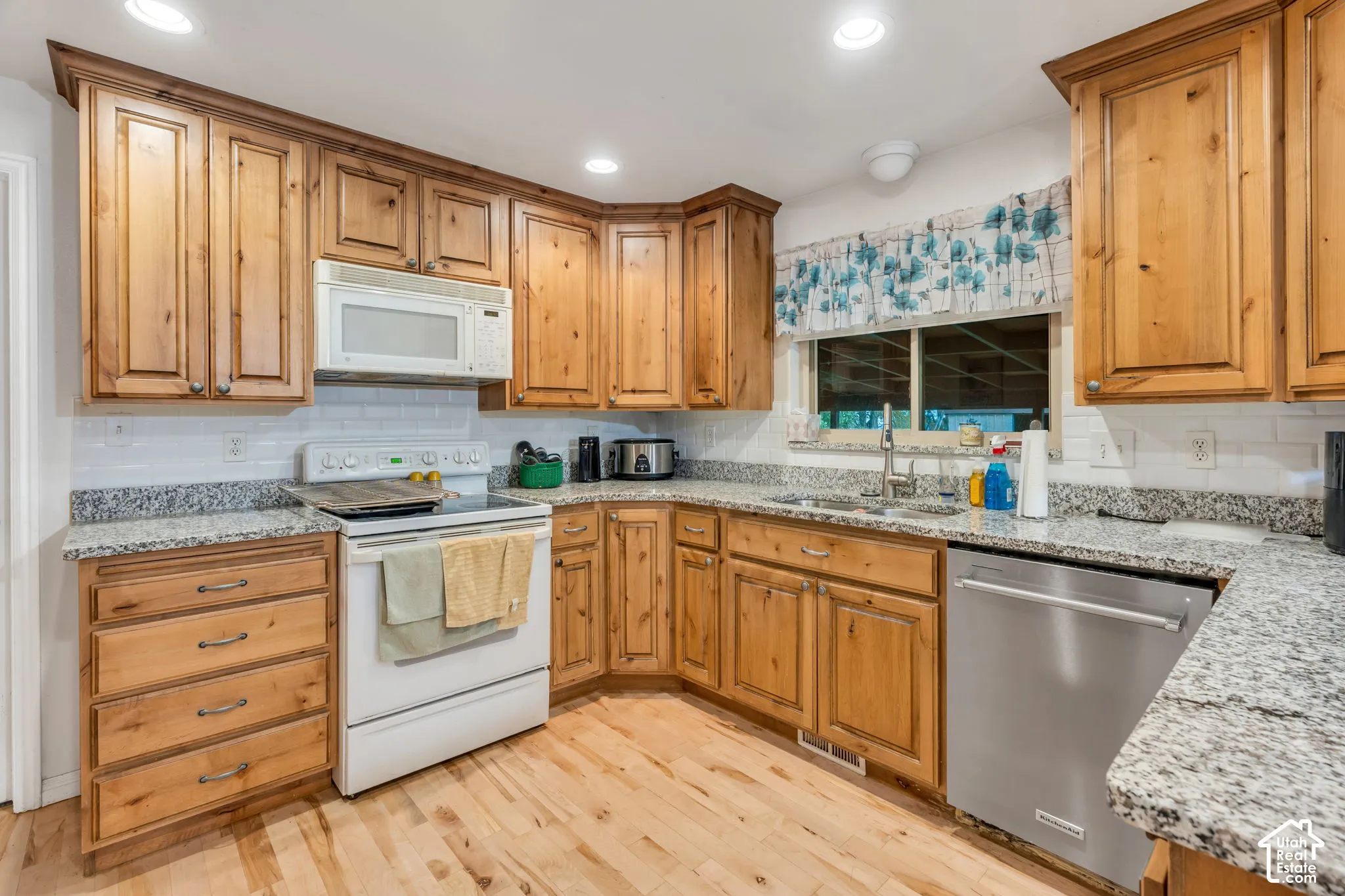 Kitchen featuring knotty wood cabinetry, light-toned stone-finish countertops, white subway tile backsplash, stainless steel dishwasher, and wood-finish flooring