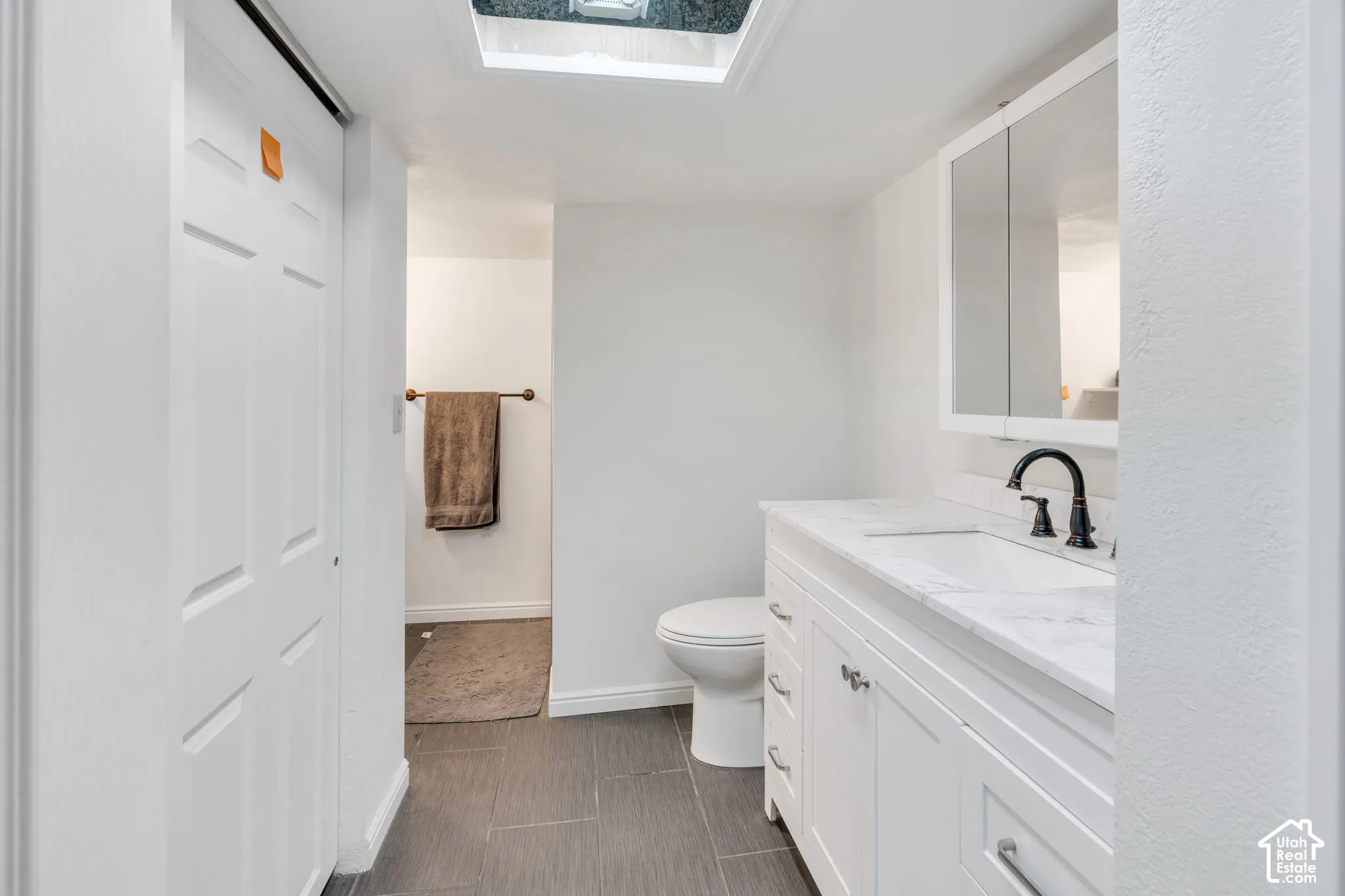 White vanity with stone-finish countertop, integrated sink, matte black faucet, mirrored medicine cabinet, and tiled flooring