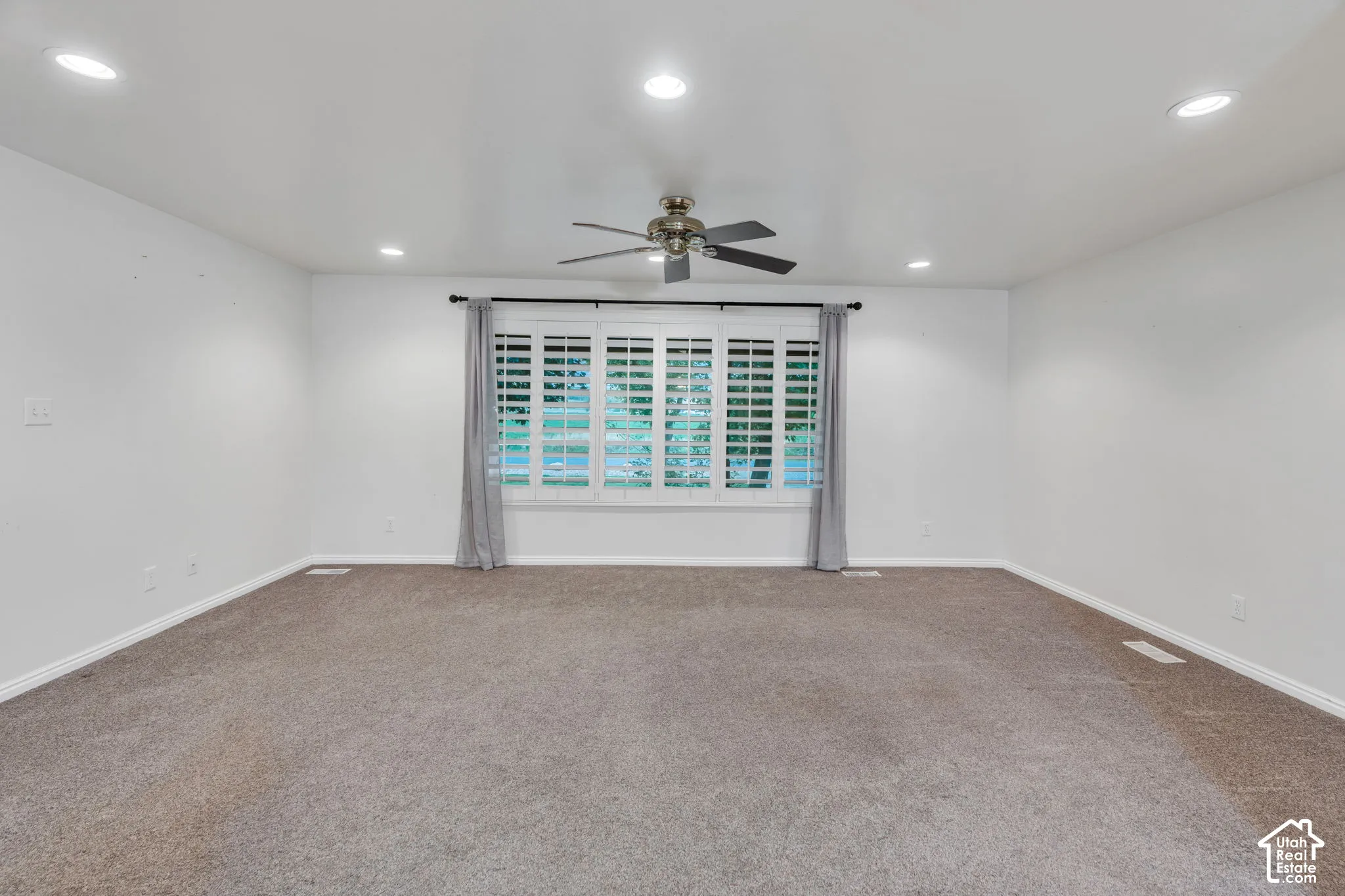 Neutral-toned room featuring recessed lighting, a ceiling fan with integrated lighting, and a large window adorned with interior plantation shutters
