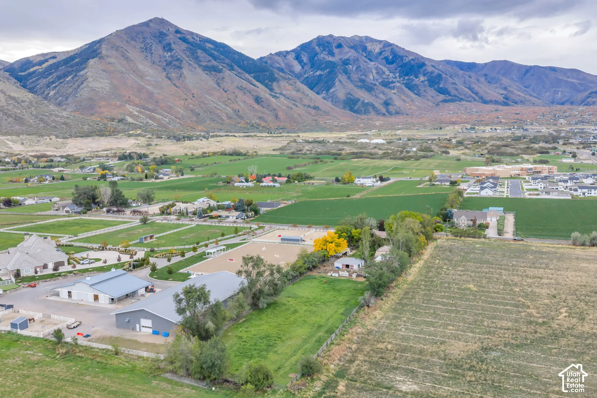 Aerial property featuring mountain backdrop, multiple outbuildings, fenced pastures, and an outdoor arena