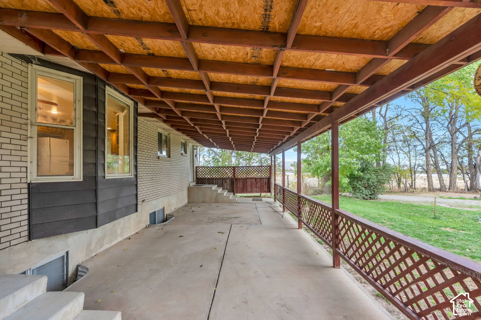 Covered concrete patio featuring exposed beam ceiling, lattice railing, and masonry siding