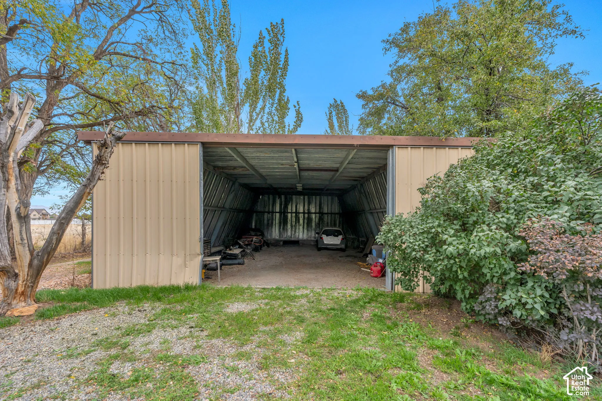 Detached metal-sided structure featuring a wide, open-bay entry and gravel flooring