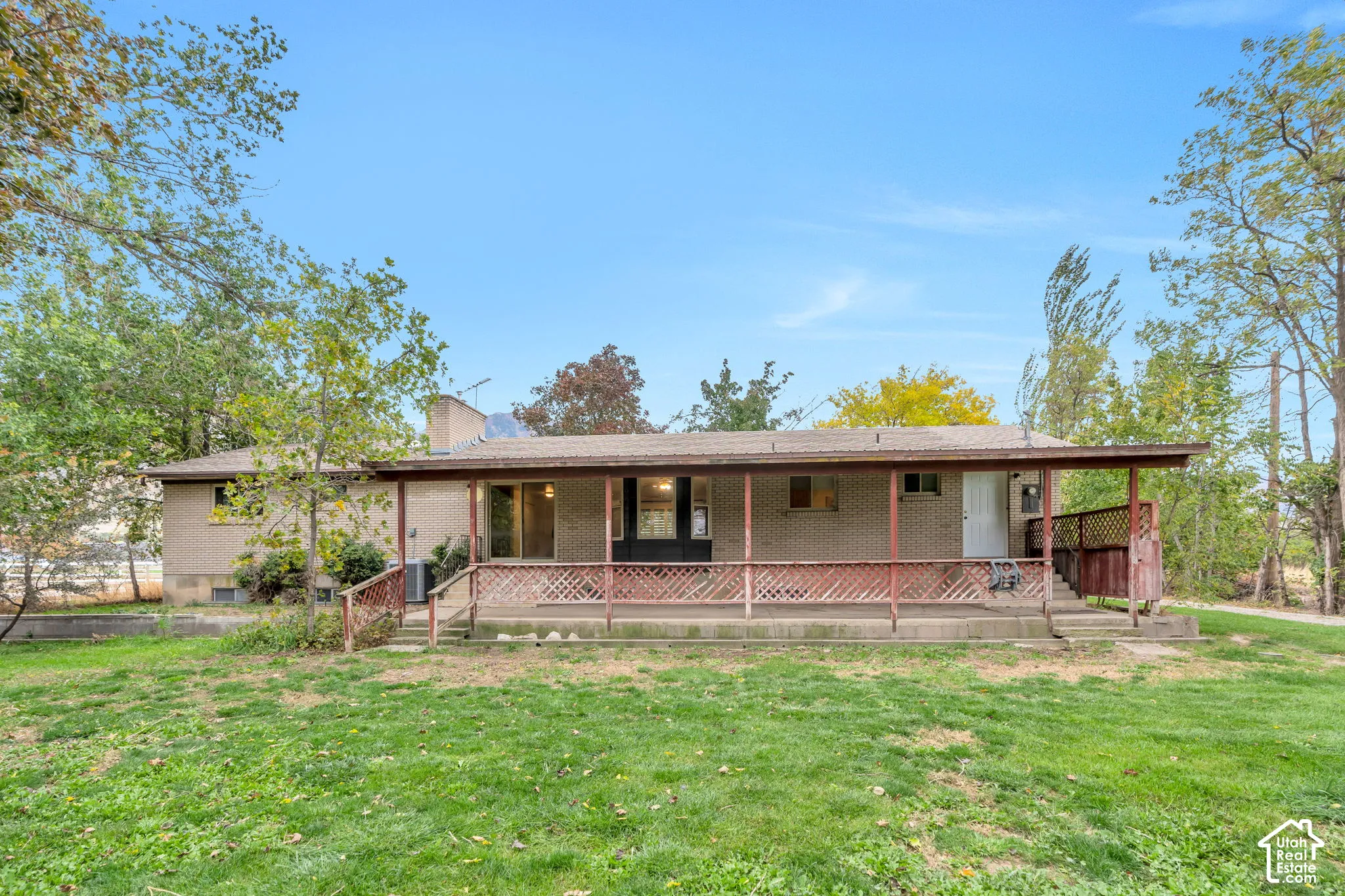 Brick exterior featuring a covered deck with wooden lattice railing and an expansive lawn