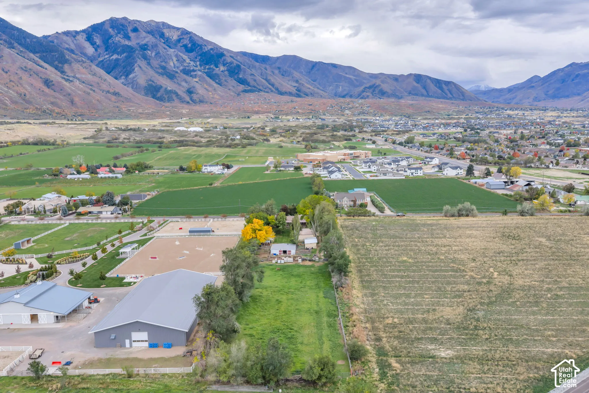 Expansive acreage featuring a metal-roofed equestrian arena, fenced outdoor riding spaces, multiple outbuildings, and a prominent mountain backdrop