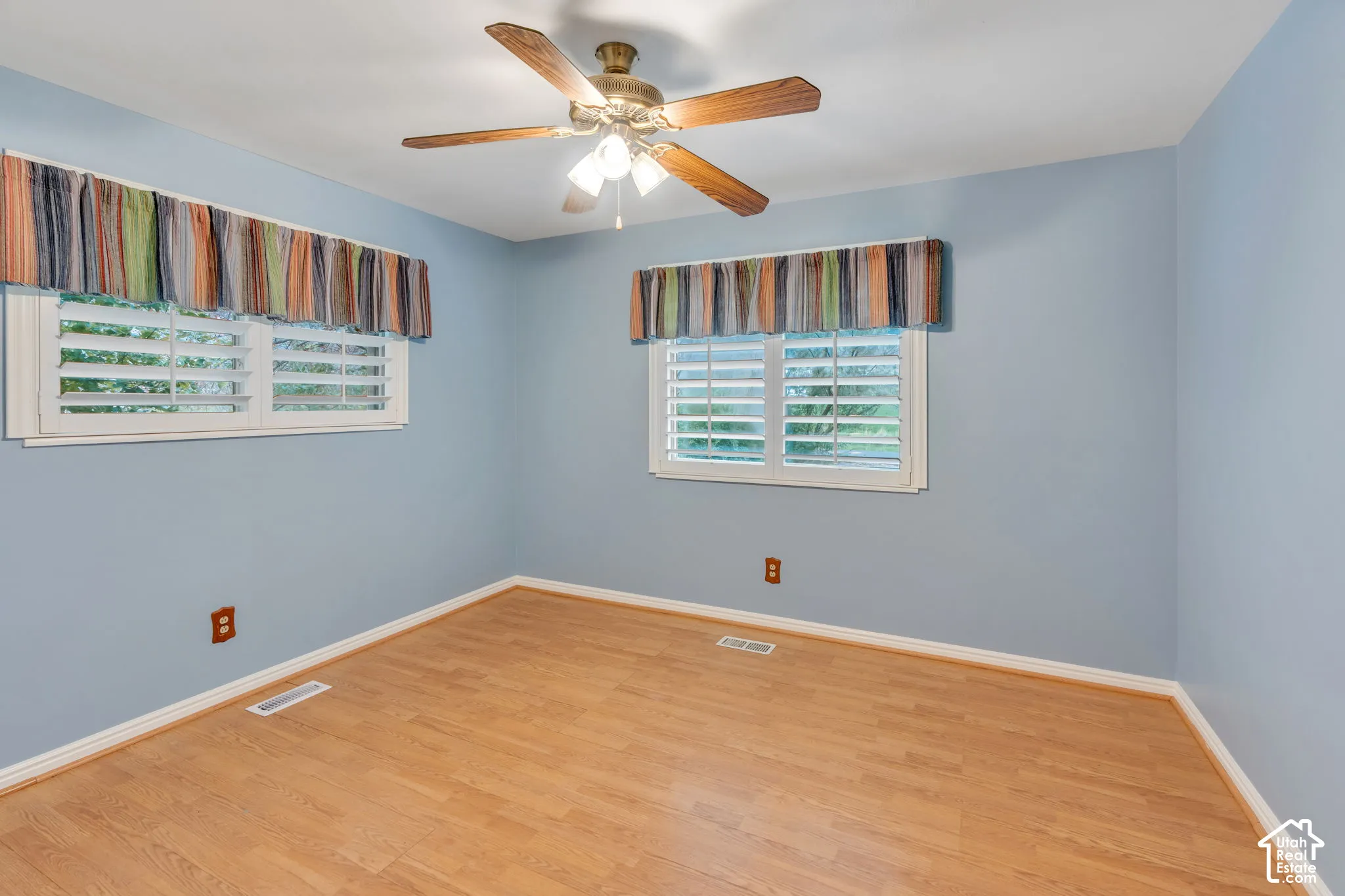 Room featuring wood-finish flooring, white plantation shutters, and a central ceiling fan with integrated lighting