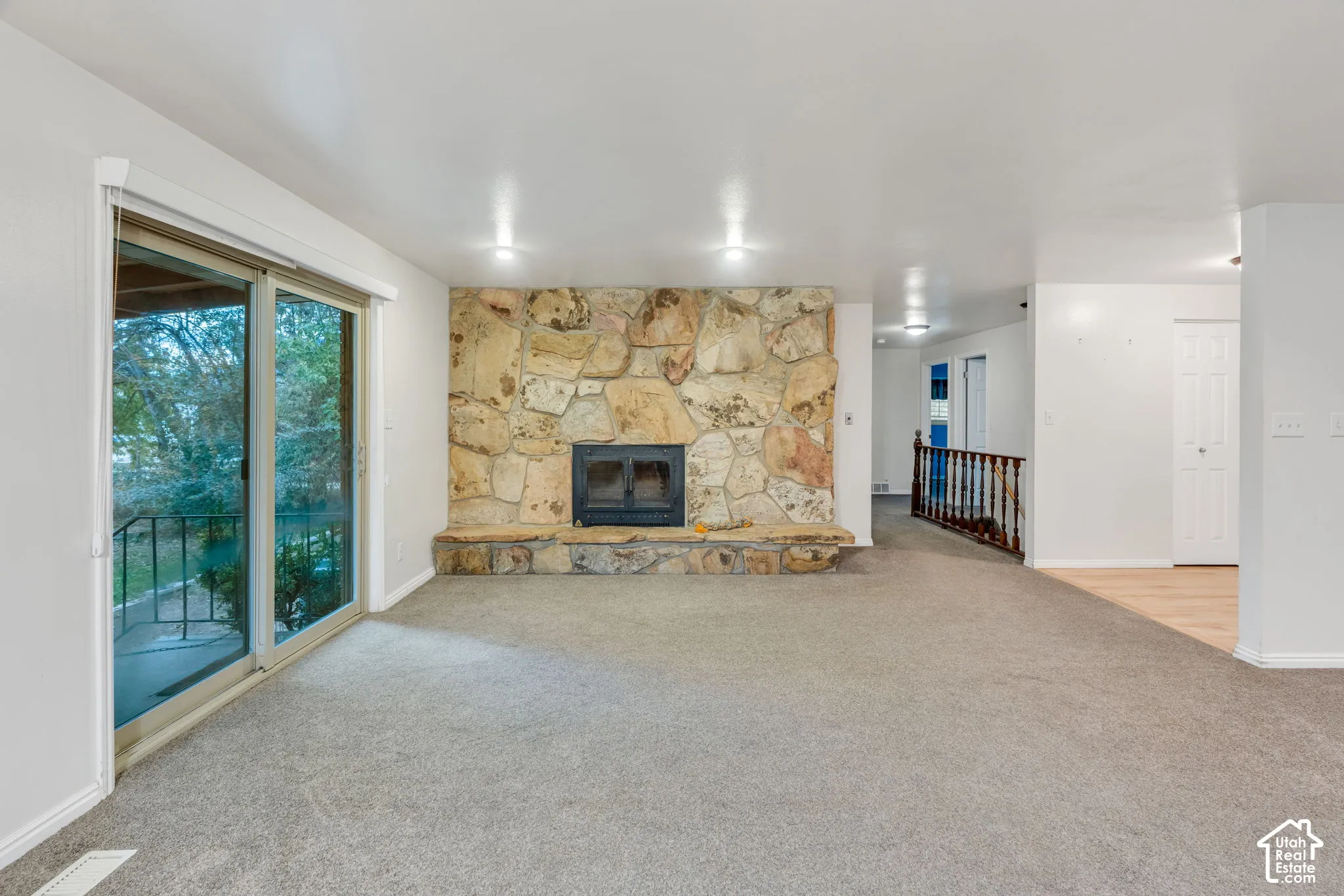 Floor-to-ceiling stone hearth with a fireplace insert, glass sliding door, recessed lighting, and wooden handrail with balusters