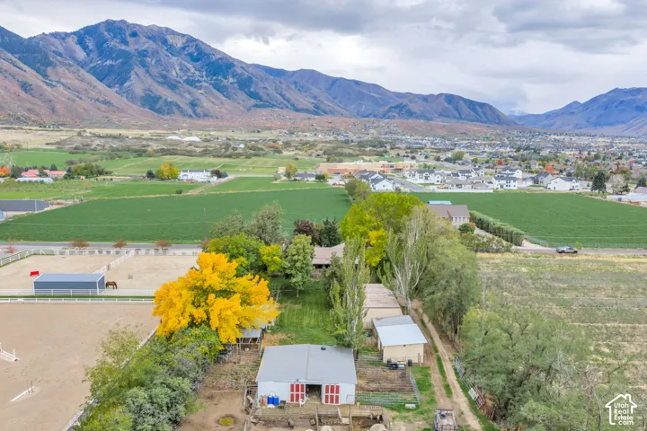 Equestrian facility featuring expansive fenced riding arenas, multiple outbuildings, mature trees, and mountainous terrain