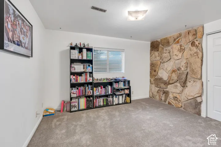 Room featuring an accent wall with natural stone masonry, neutral carpeting, and a window with horizontal blinds