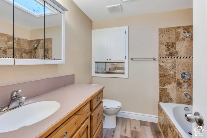 Bathroom featuring wood-finish flooring, a wood vanity with a solid-surface countertop, a mirrored medicine cabinet, built-in cabinetry, and a tub-shower combination with natural stone-tiled surround