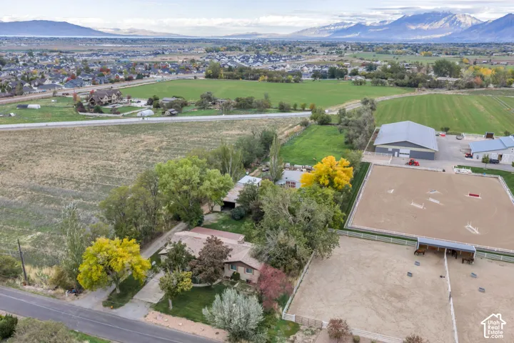 Aerial perspective of an expansive property featuring fenced equestrian arenas, a multi-bay detached outbuilding, mature trees, and mountain surroundings