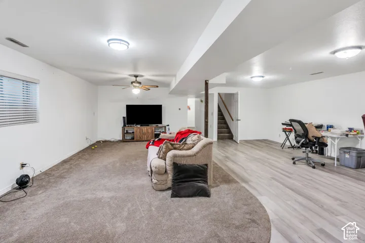Expansive lower-level space featuring wood-finish flooring, wall-to-wall carpeting, a central ceiling fan with integrated lighting, and flush-mount ceiling fixtures