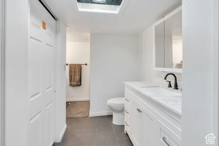 White vanity with stone-finish countertop, integrated sink, matte black faucet, mirrored medicine cabinet, and tiled flooring