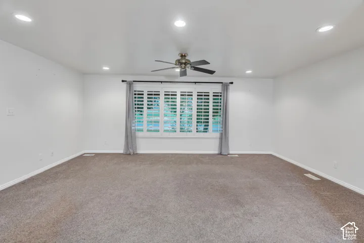Neutral-toned room featuring recessed lighting, a ceiling fan with integrated lighting, and a large window adorned with interior plantation shutters