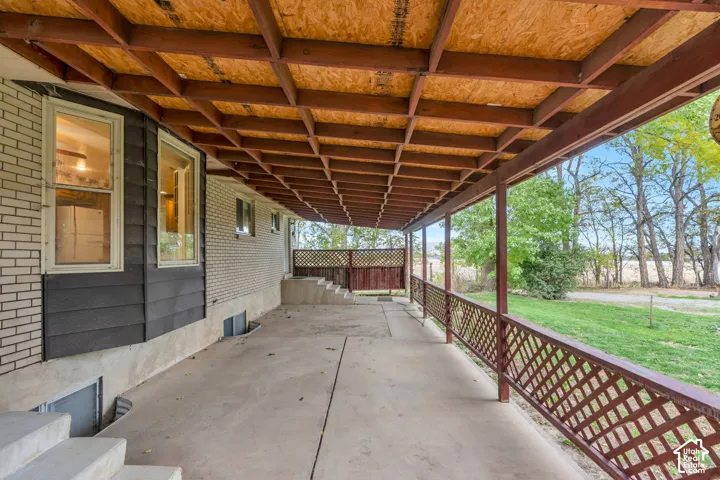 Covered concrete patio featuring exposed beam ceiling, lattice railing, and masonry siding