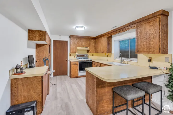 Kitchen featuring wood cabinetry, solid surface countertops, a peninsula with bar seating space, and wood-finish flooring