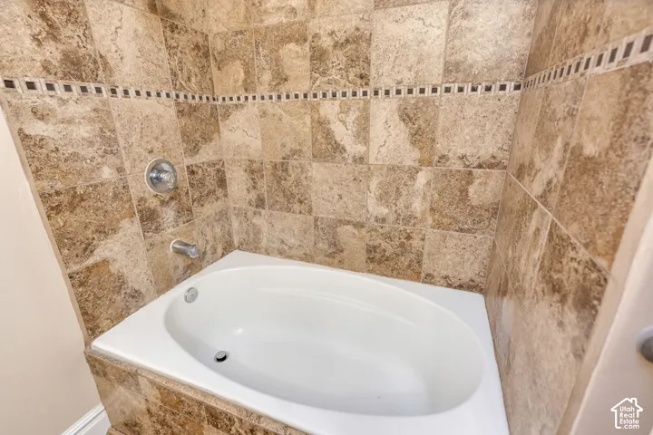 Built-in oval soaking tub surrounded by stone-finish tile, decorative mosaic tile accent border, and chrome plumbing fixtures