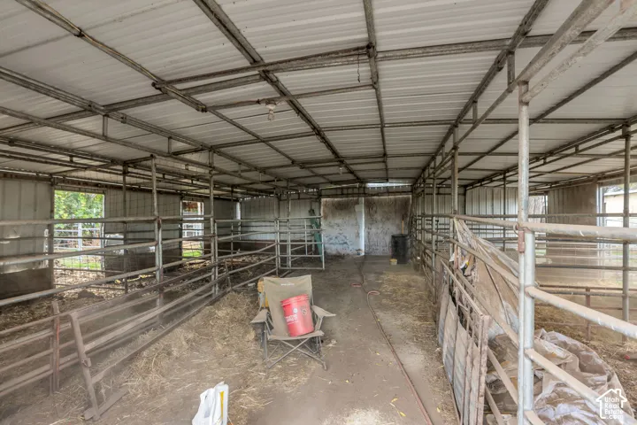 Covered livestock shelter featuring a metal roof structure, individual partitioned stalls with tubular steel fencing, and dirt flooring