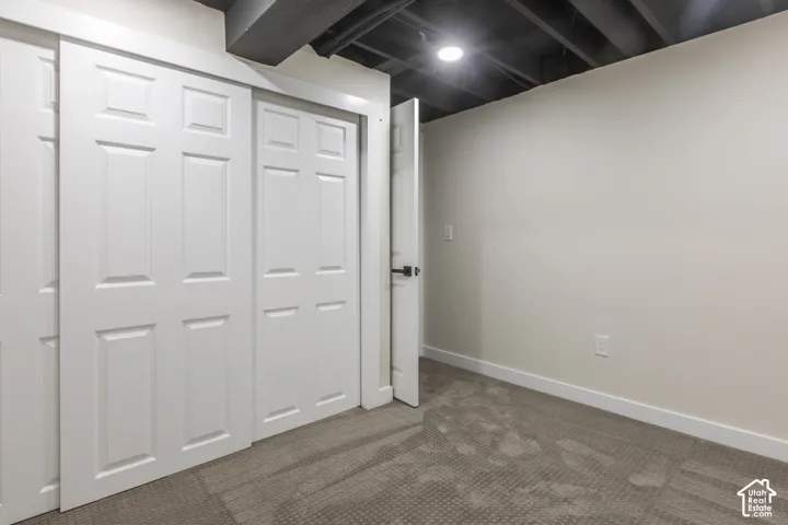 Neutral-toned room featuring a sliding multi-panel closet door, recessed ceiling lighting, exposed painted ceiling joists, and wall-to-wall carpeting