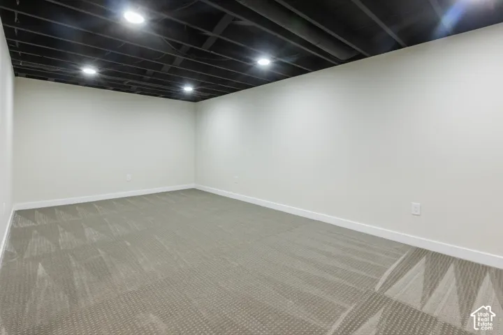 Interior space featuring neutral wall tones, high-density patterned carpeting, and an exposed ceiling finished in matte black with recessed lighting