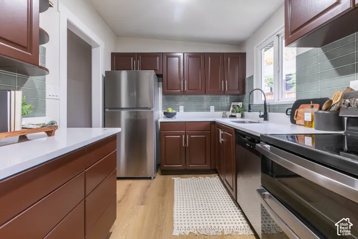 Kitchen featuring dark-toned cabinetry, solid-surface white countertops, a green subway tile backsplash, wood-finish flooring, and stainless steel appliances