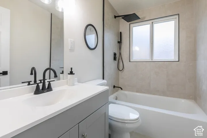 Bathroom featuring a gray vanity with a white countertop, matte black fixtures, a tiled tub-shower surround, and a rectangular window