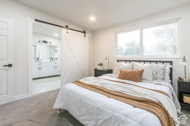 Bedroom interior featuring neutral wall paint, carpet flooring, a large window, and a white sliding barn-style door opening to a vanity area with dual sinks