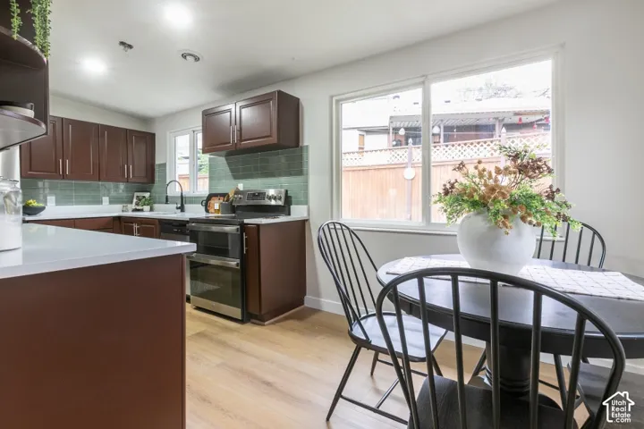 Kitchen featuring stained cabinetry, white countertops, green subway tile backsplash, stainless steel range, and wood-finish flooring
